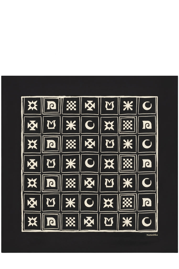 A square black silk scarf  featuring a cream-colored grid of various geometric and celestial motifs, including stars, moons, and checkered squares. The brand name 'Nanushka' is printed in small cream text in the bottom right corner.