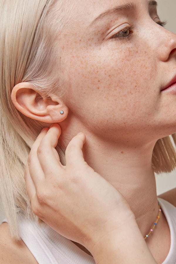 Model wearing the dot stud single earring in gold and icy-blue colour from the brand ENAMEL COPENHAGEN