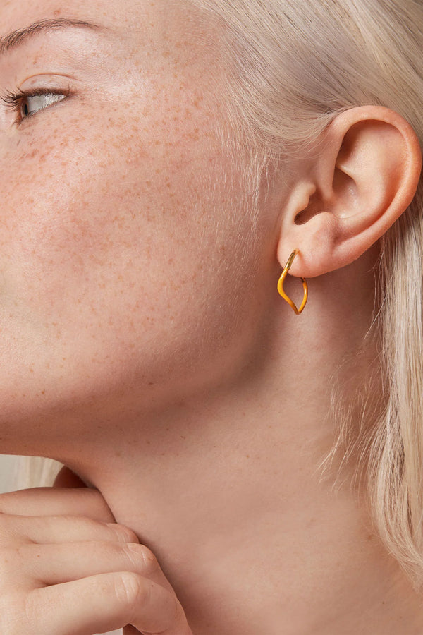 Model wearing the Sway hoop earrings in gold and orange colours from the brand ENAMEL COPENHAGEN